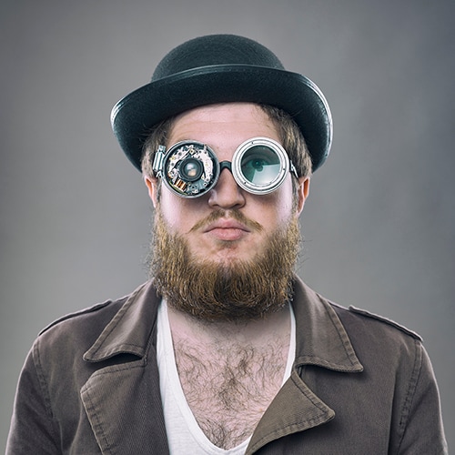 bearded caucasian man wearing a bowler hat and steampunk glasses
